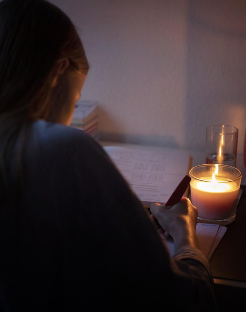 Frau schreibt bei Kerzenlicht in ihrem ansonsten dunklen Zuhause