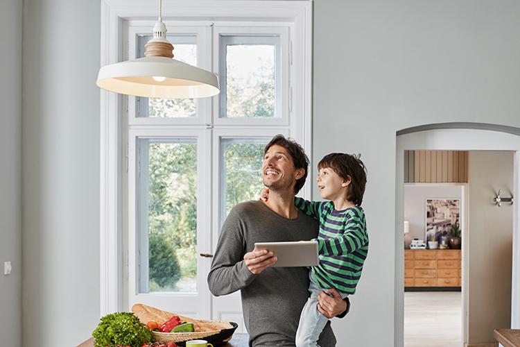 Vater mit Tablet in der Hand und Sohn auf dem Arm schauen eine Lampe an.