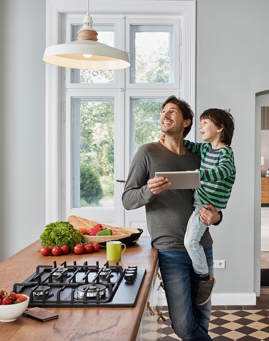 Vater mit Tablet in der Hand und Sohn auf dem Arm schauen eine Lampe an.