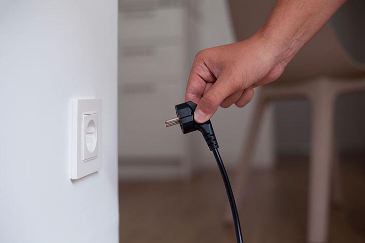 Eine Hand steckt schwarzen Stecker in eine Steckdose