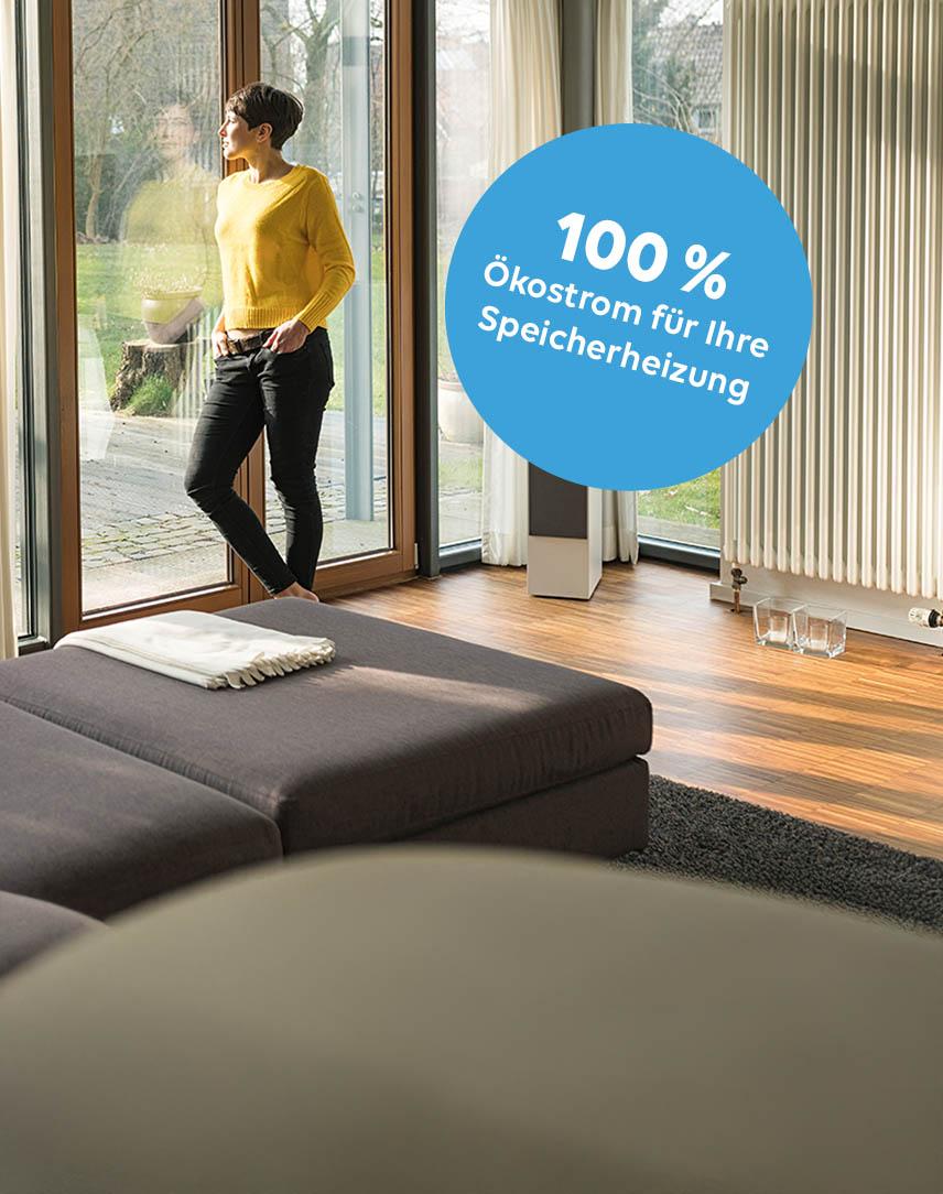 Frau steht am Fenster und schaut in ihren sonnendurchfluteten Garten