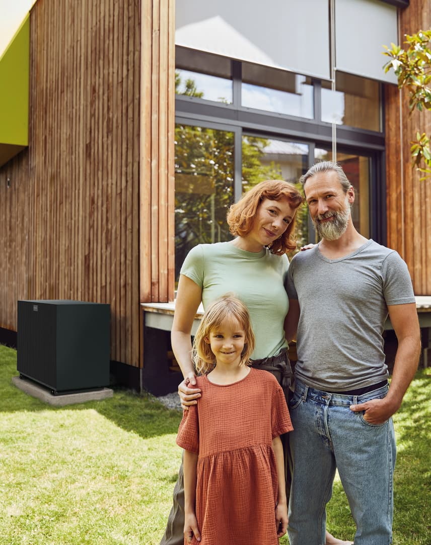 Familie steht vor Ihren Haus, neben dem sich eine Wärmepumpe befindet