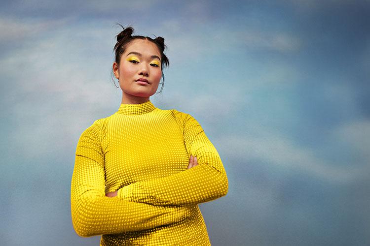 Frau mit verschränkten Armen vor Himmel-Hintergrund.