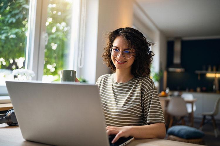 Junge Frau sitzt im Wohnzimmer an Laptop