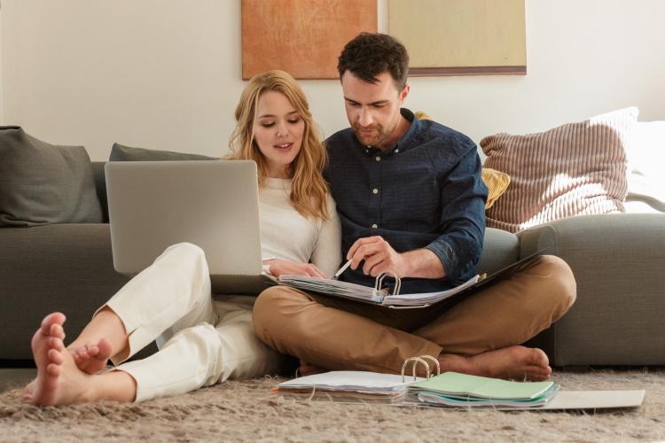 Ein Paar sitzt auf dem Boden und schaut in einen Laptop bzw. einen Aktenordner