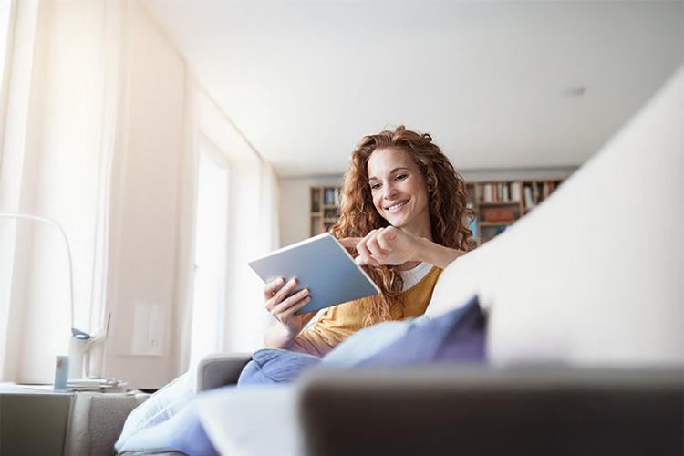 Frau sitzt auf Sofa und schaut glücklich auf Tablet