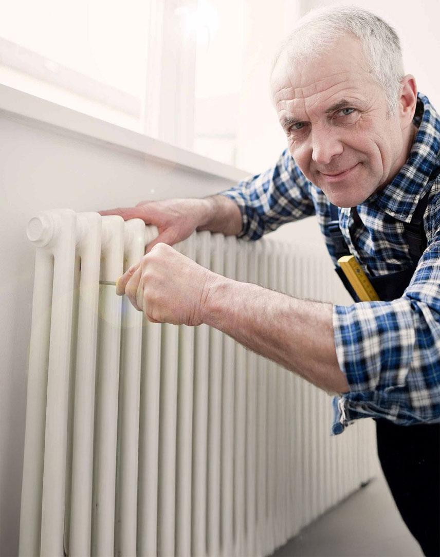 Mann im karierten Hemd werkelt an einer Heizung