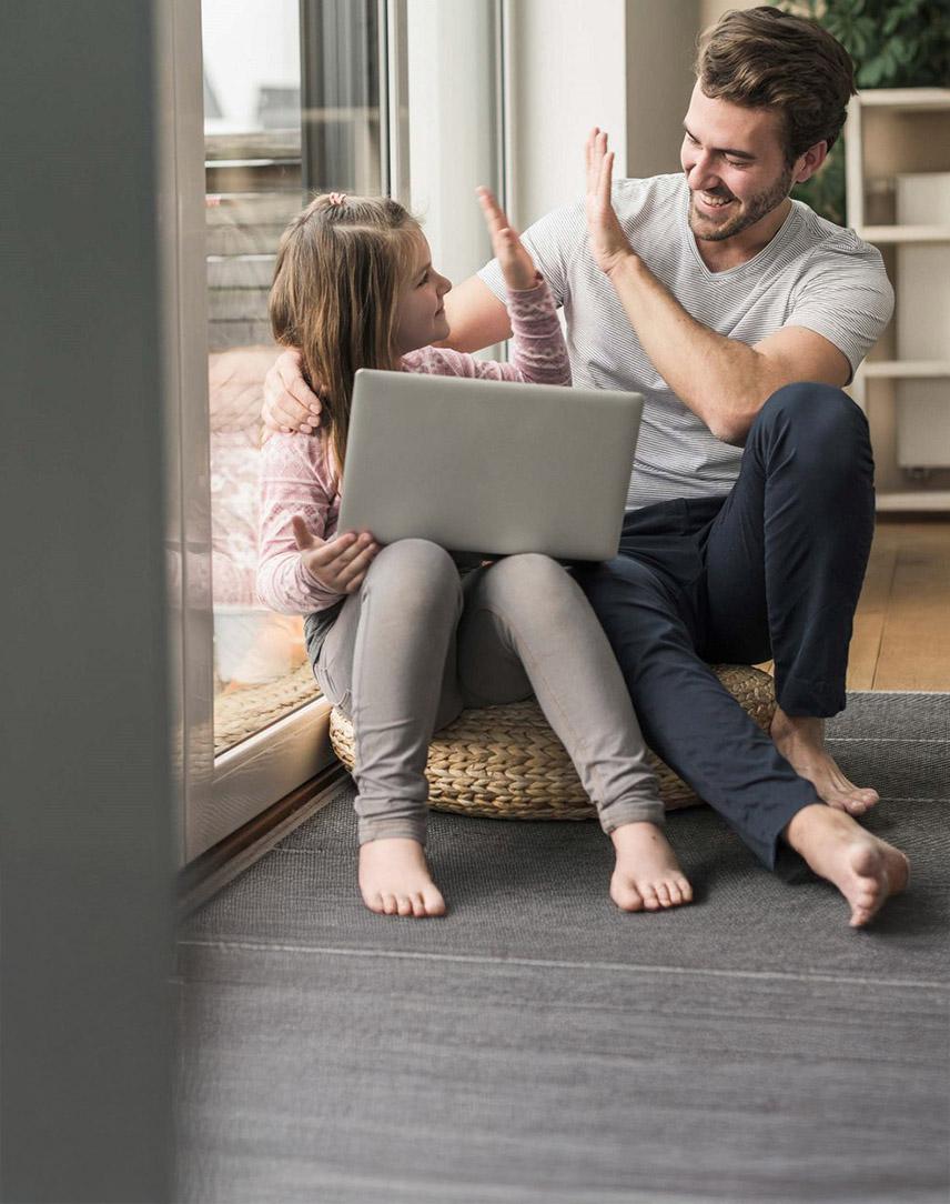 Vater und Tochter mit Laptop auf dem Schoß geben sich ein High-Five