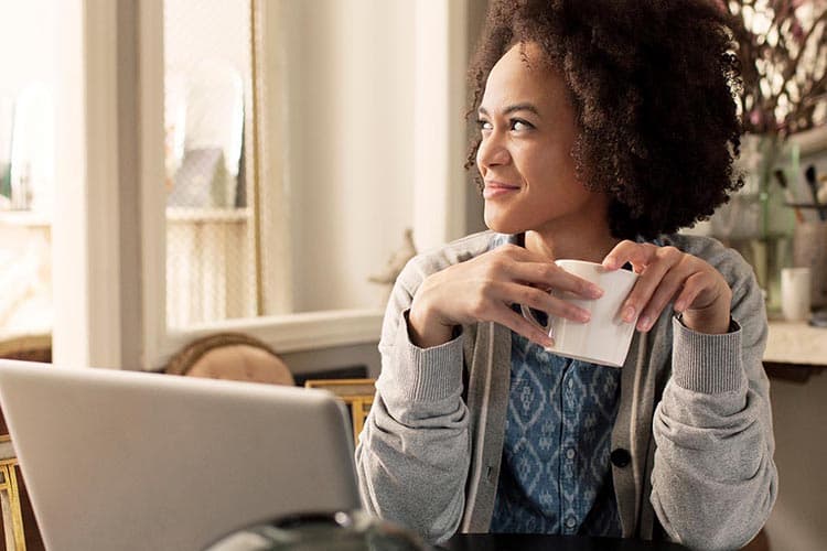 Frau vor dem Laptop schaut lächelnd aus dem Fenster