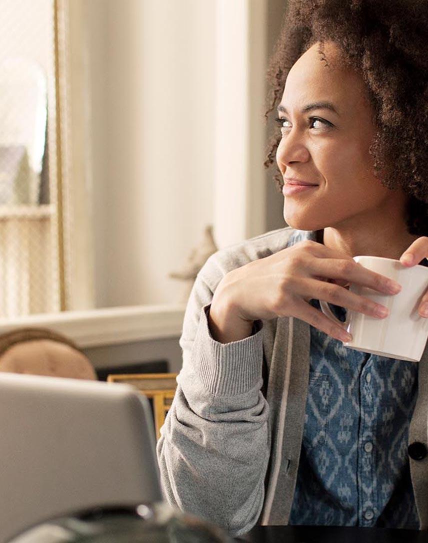 Frau vor dem Laptop schaut lächelnd aus dem Fenster