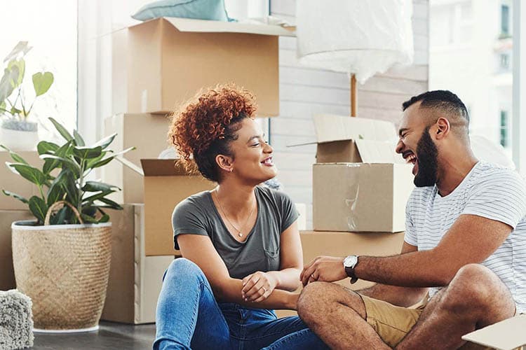 Lachendes Pärchen sitzt vor Umzugskantons auf dem Boden