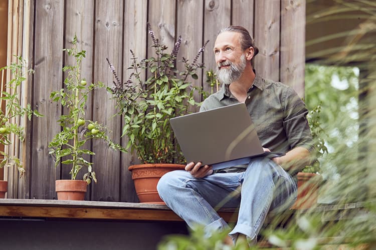 Mann sitzt mit Laptop auf dem Schoß auf der Terrasse