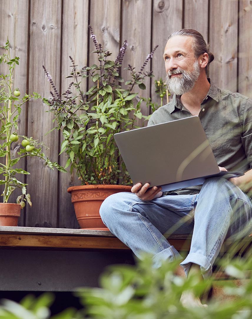 Mann sitzt mit Laptop auf dem Schoß auf der Terrasse