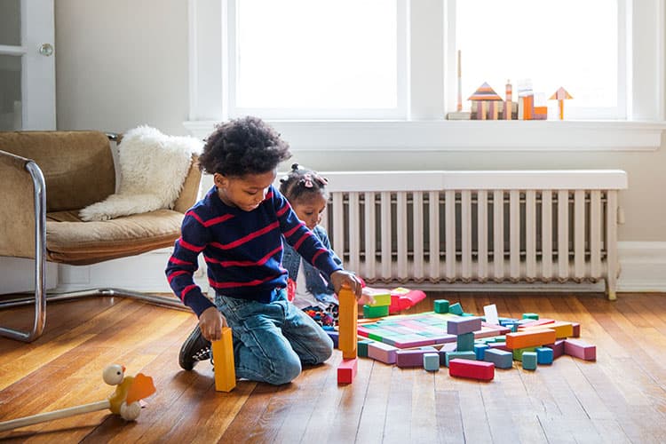 Junge spielt mit Bauklötzen im Wohnzimmer vor einer Heizung