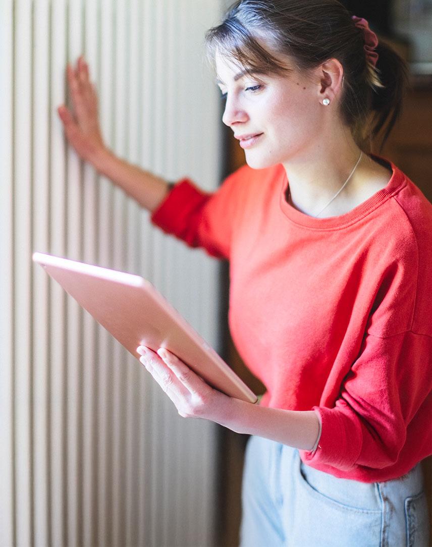 Frau schaut auf ihr Tablet und fühlt die Temperatur der Heizung