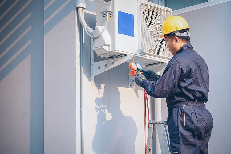 Handwerker mit Bauhelm installiert eine Wärmepumpe an Hauswand