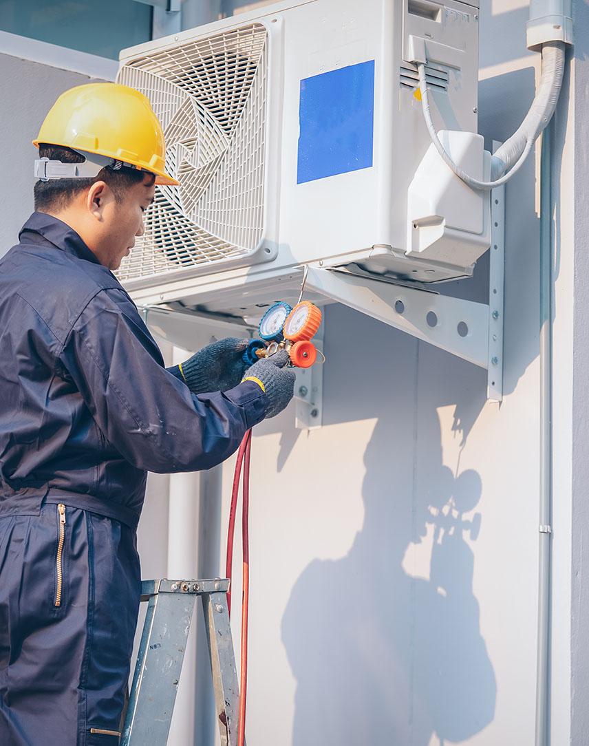 Handwerker mit Bauhelm installiert eine Wärmepumpe an Hauswand