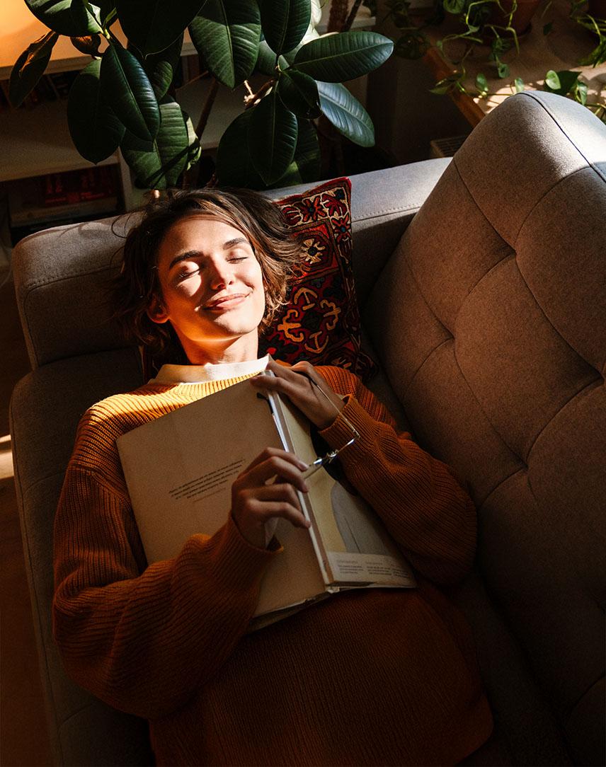 Frau liegt auf dem Sofa und wird von der Sonne angeschienen. 