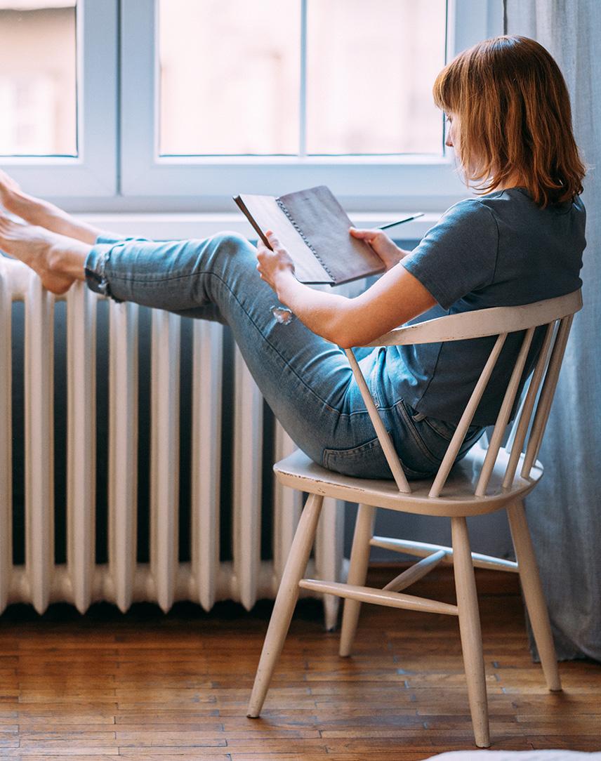 Frau liest etwas auf dem Tablet und legt dabei die Füße auf der Heizung hoch