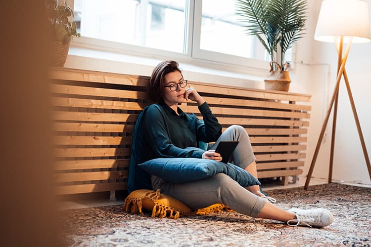 Frau lehnt mit Tablet in der Hand an Heizung