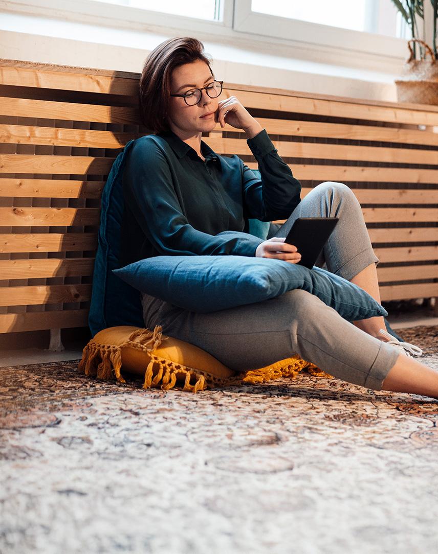 Frau lehnt mit Tablet in der Hand an Heizung