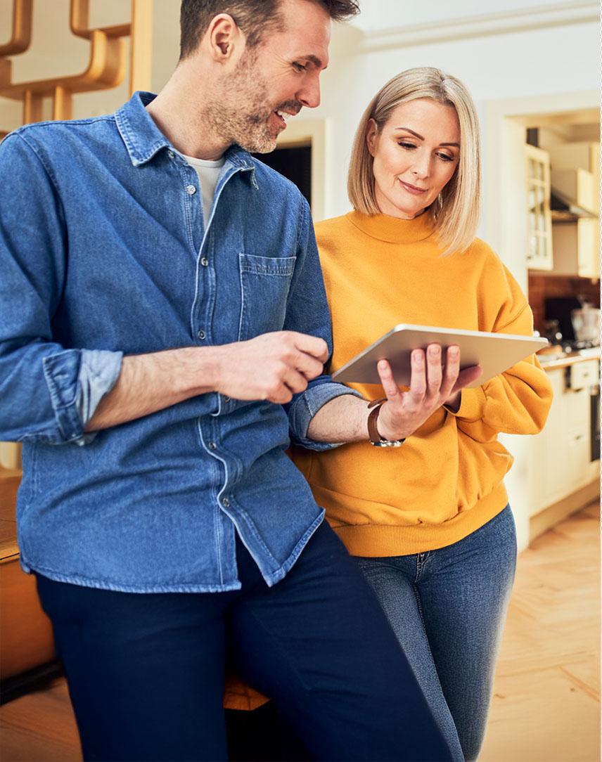 Mann und Frau stehen in der Küche und schauen auf ein Tablet