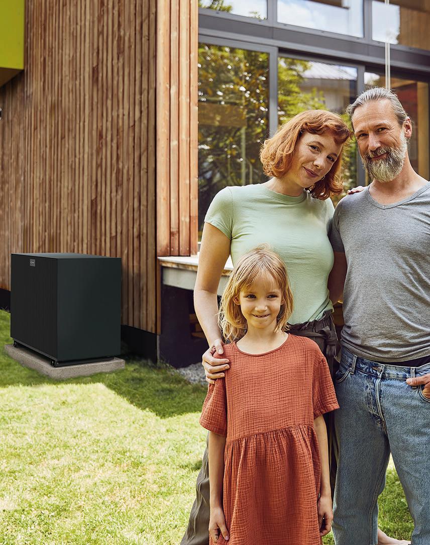 Mutter, Vater und Tochter stehen vor einem haus mit Wärmepumpe