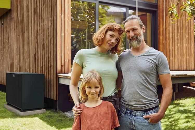 Vater, Mutter und Tochter stehen vor ihrem Haus mit Wärmepumpe