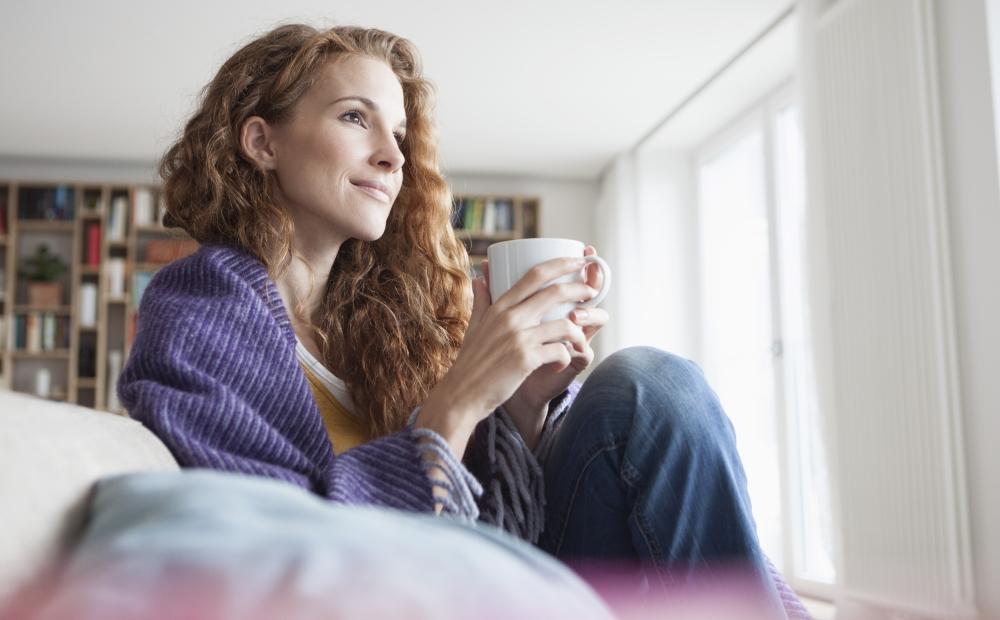 Frau sitzt entspannt in ihrem Wohnzimmer und trinkt eine Tasse Tee