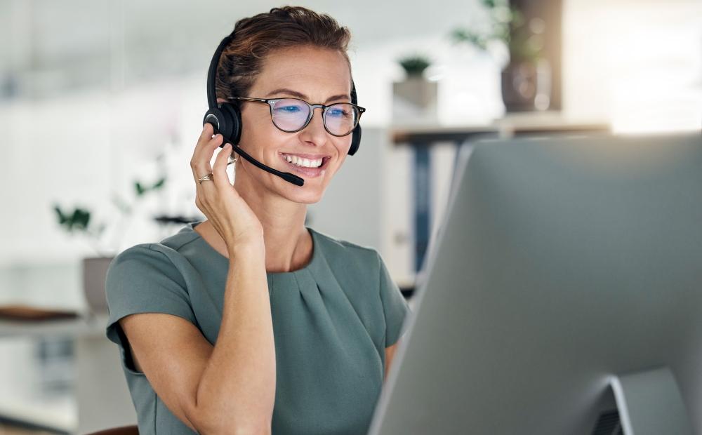 Frau sitzt vor einem Laptop und telefoniert mit Headset