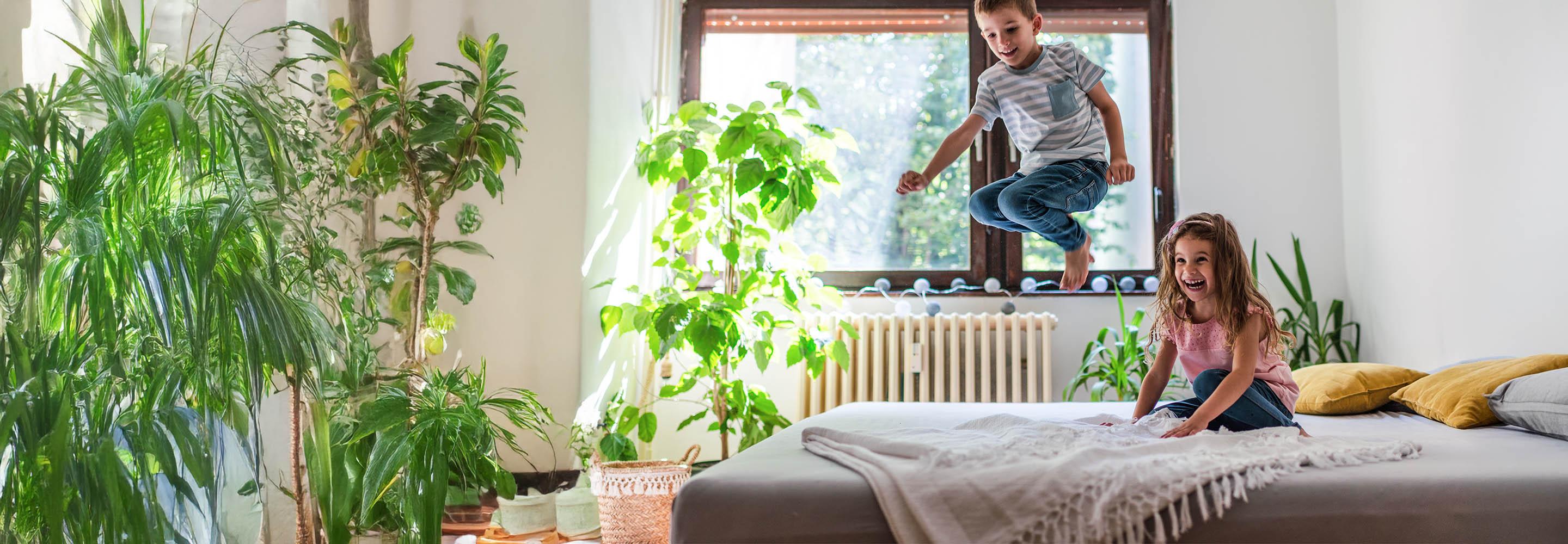 Ein kleiner Junge springt vergnügt auf einem Bett, ein kleines Mädchen schaut ihm lachend zu