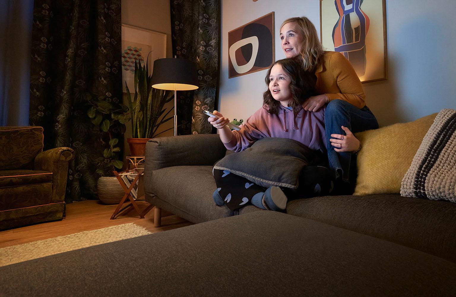 Mutter und Tochter sitzen auf der Couch mit einer Fernbedienung und schauen EWE ZuhauseTV