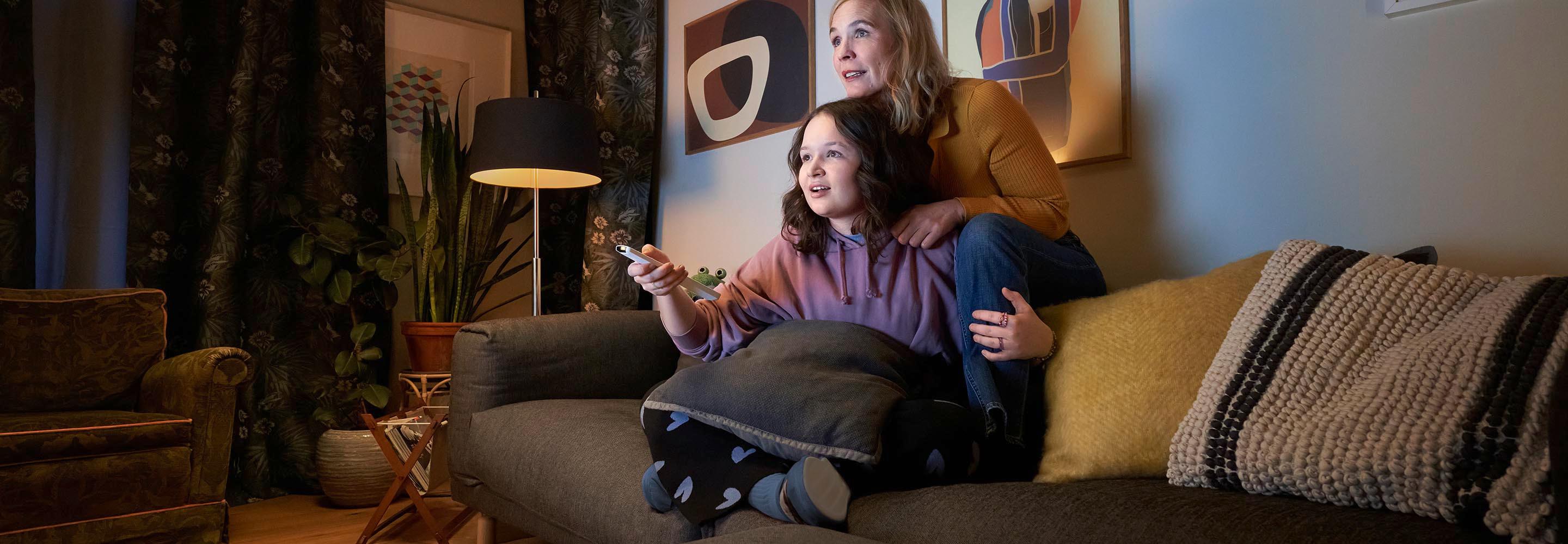 Mutter und Tochter sitzen auf der Couch mit einer Fernbedienung und schauen EWE ZuhauseTV