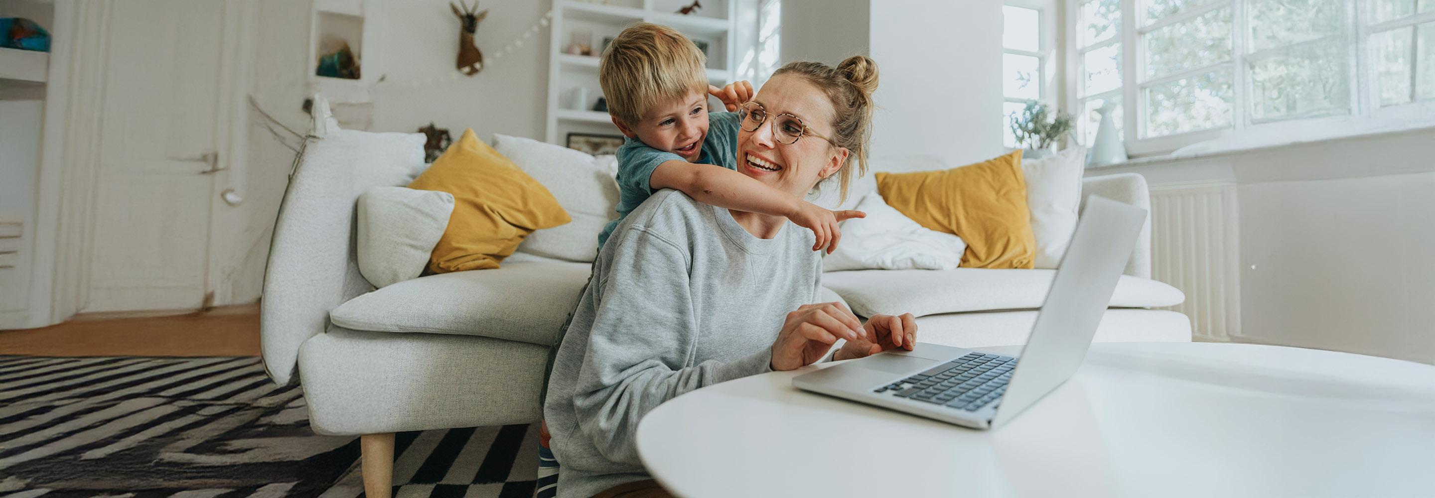Eine Frau sitzt am Laptop, ihr Sohn umarmt sie und zeigt auf den Bildschirm