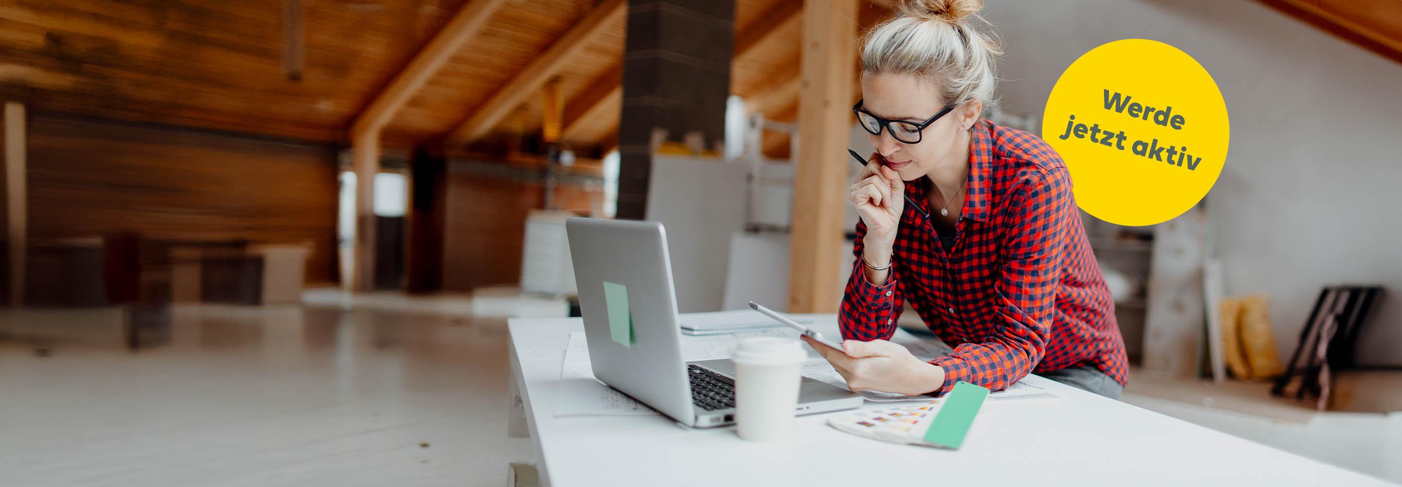 Frau am Schreibtisch vor Laptop schaut aufs Smartphone