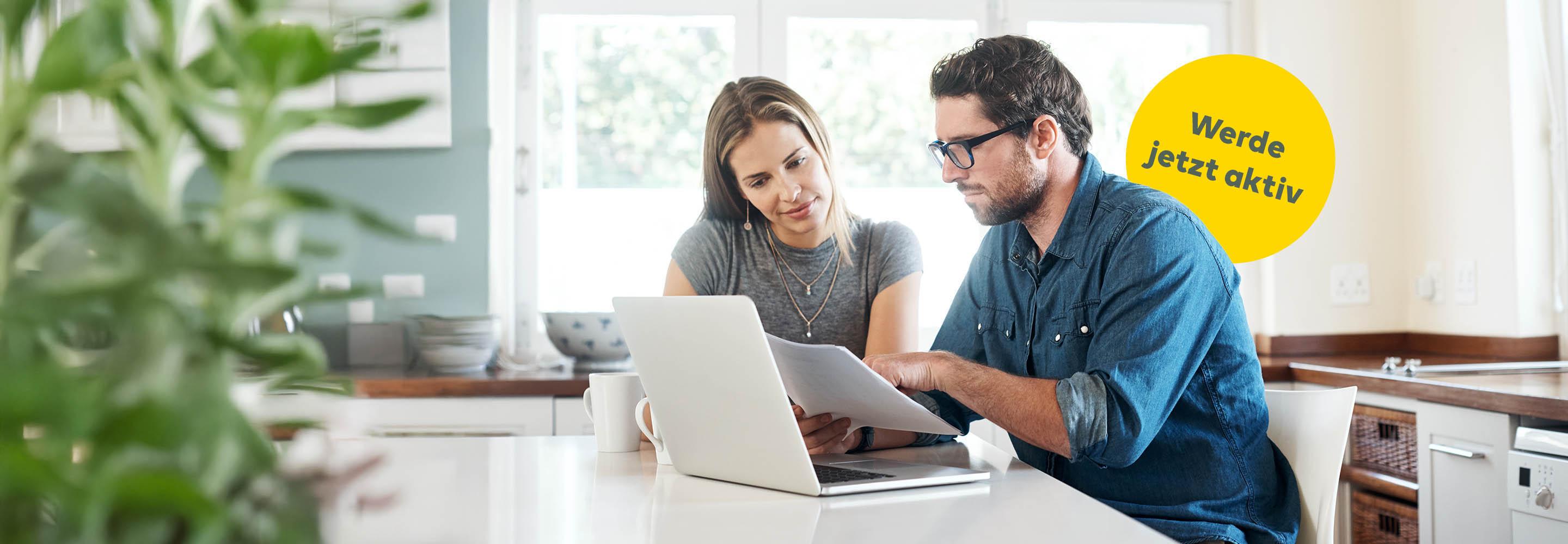 Frau und Mann sitzen vor Laptop mit Unterlagen in der Hand