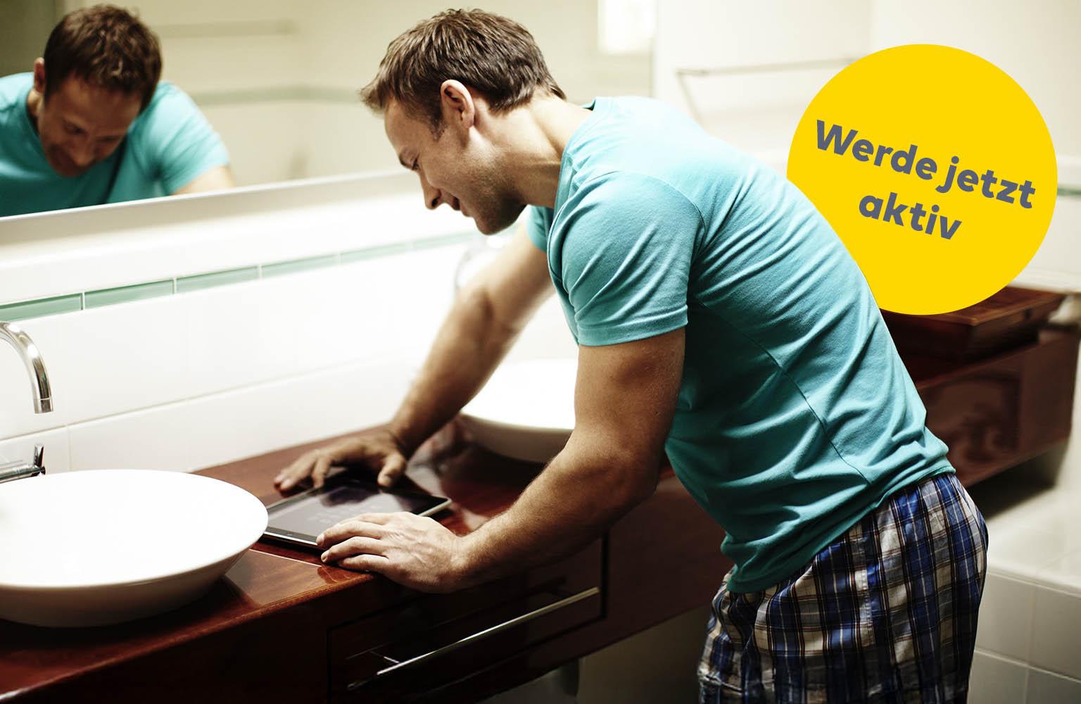 Mann schaut im Badezimmer auf Tablet