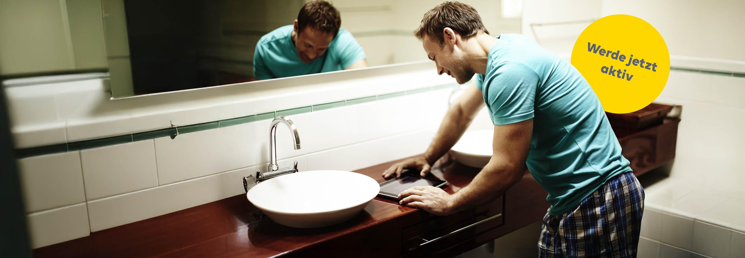 Mann schaut im Badezimmer auf Tablet