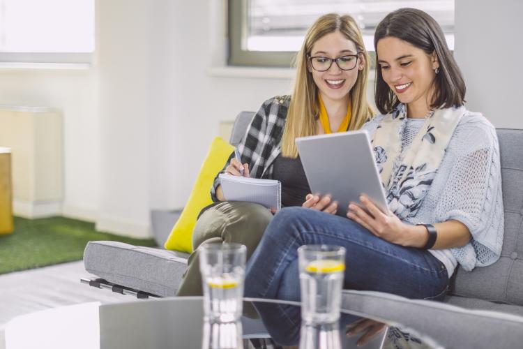 Zwei Frauen unterhalten sich und schauen auf Zettel bzw. einen Laptop