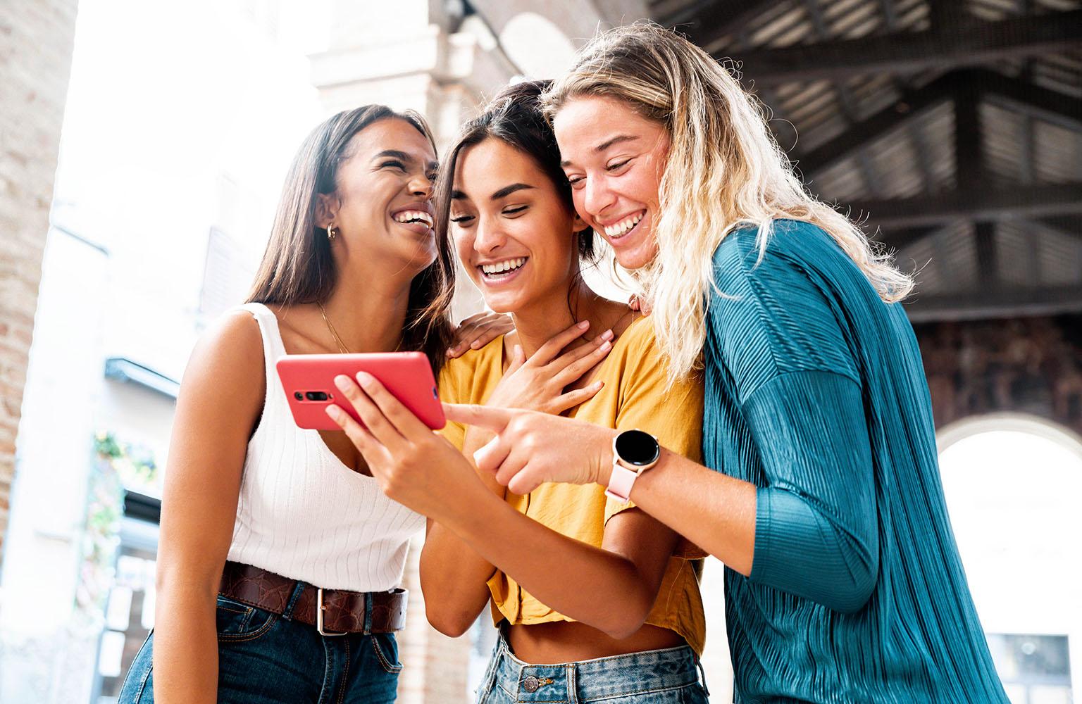 Drei Frauen schauen lachend auf ein Smartphone
