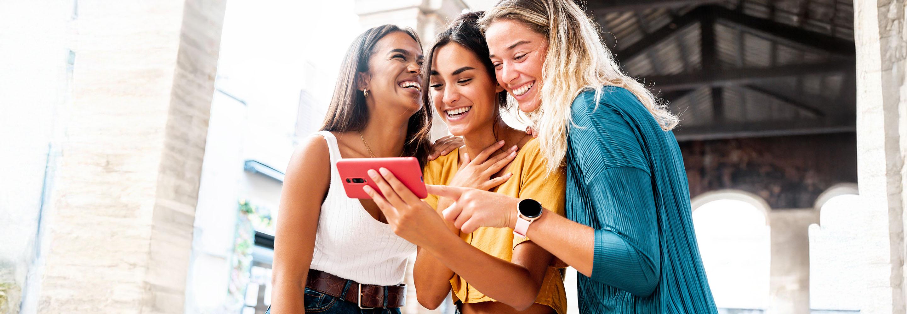 Drei Frauen schauen lachend auf ein Smartphone