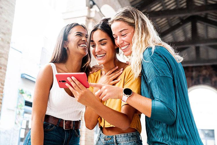 Drei Frauen schauen lachend auf ein Smartphone