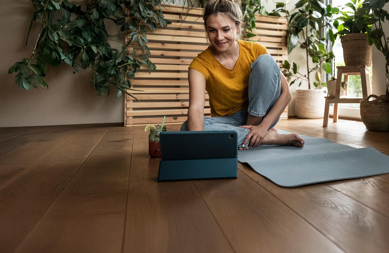 Lächelnde Frau auf Yogamatte schaut auf ihr Tablet