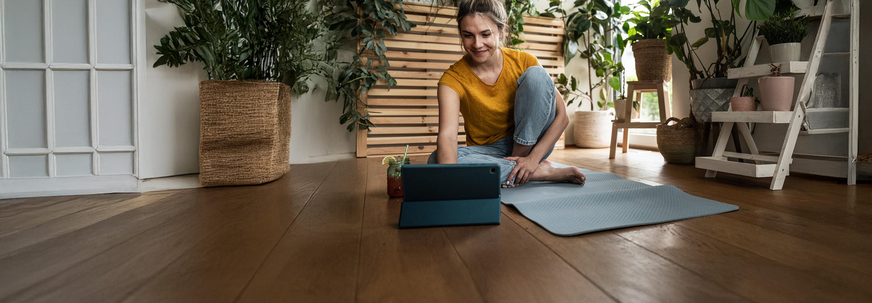 Lächelnde Frau auf Yogamatte schaut auf ihr Tablet