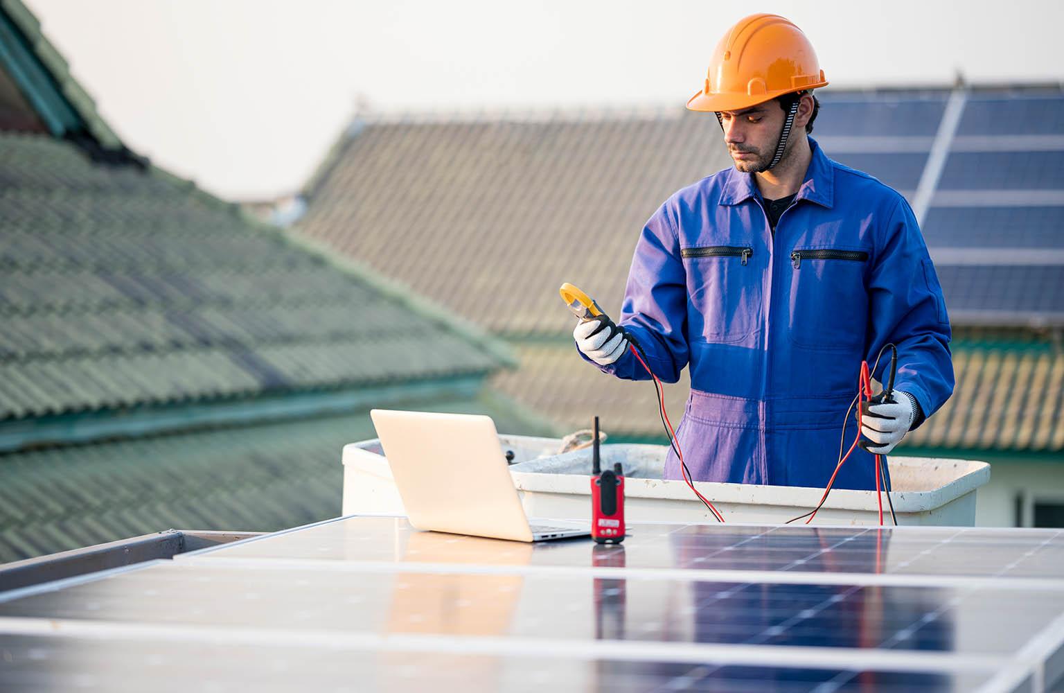 Mann mit Helm prüft die Leistung eines PV-Moduls auf Dach