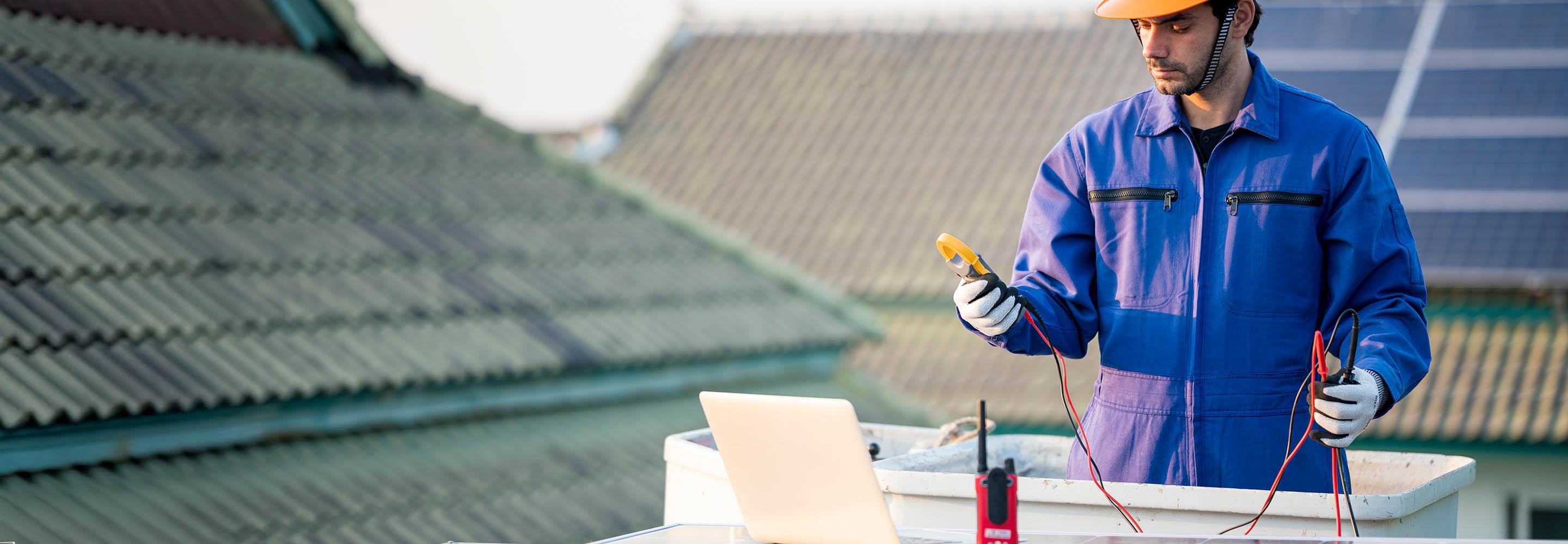 Mann mit Helm prüft die Leistung eines PV-Moduls auf Dach