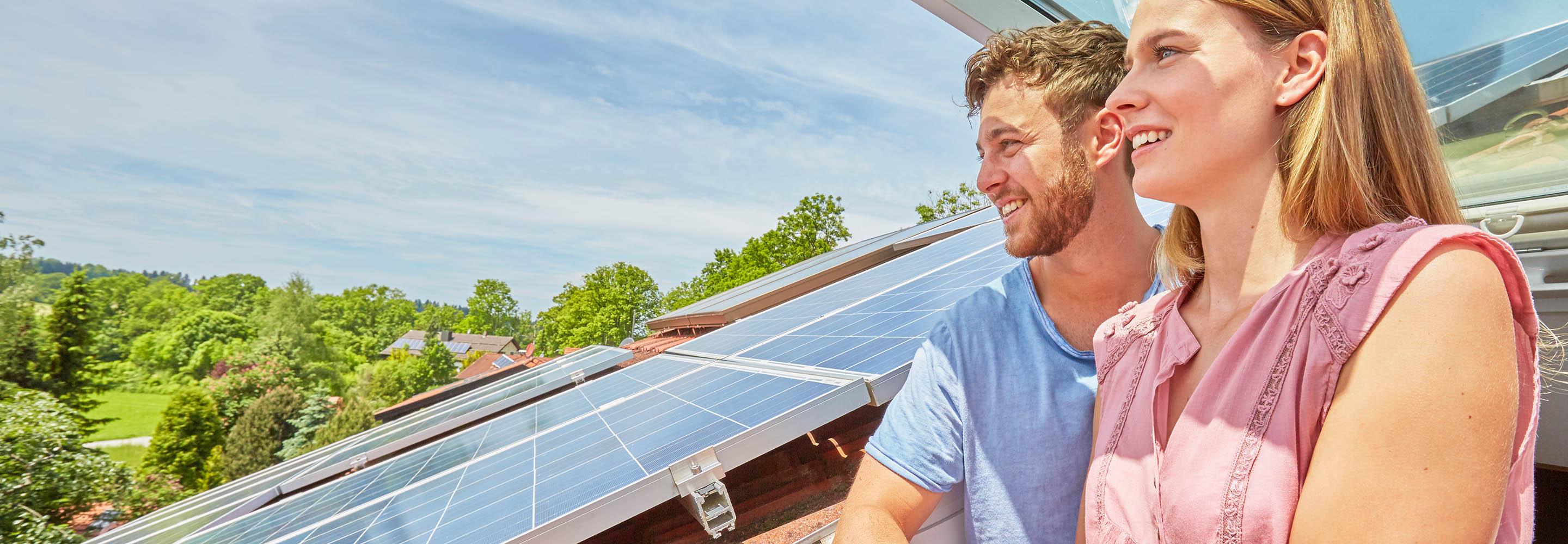 Mann und Frau schauen aus einem Dachfenster, daneben sind PV-Module sichtbar