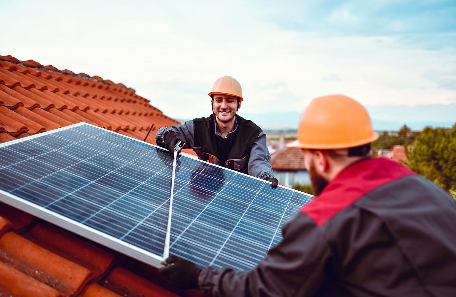 Zwei Männer mit Helm montieren PV-Modul auf einem Dach