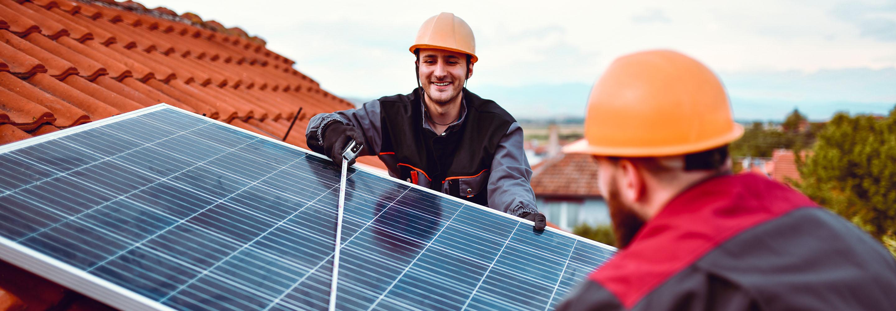 Zwei Männer mit Helm montieren PV-Modul auf einem Dach