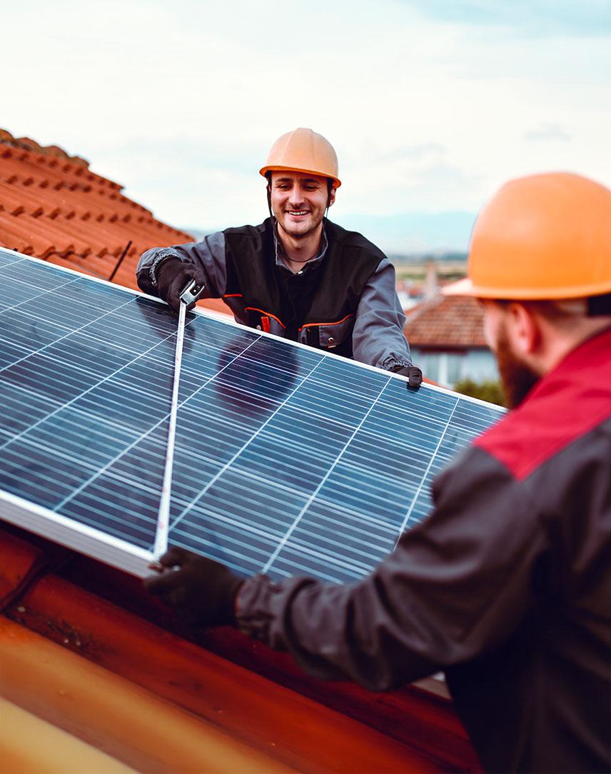 Zwei Männer mit Helm montieren PV-Modul auf einem Dach